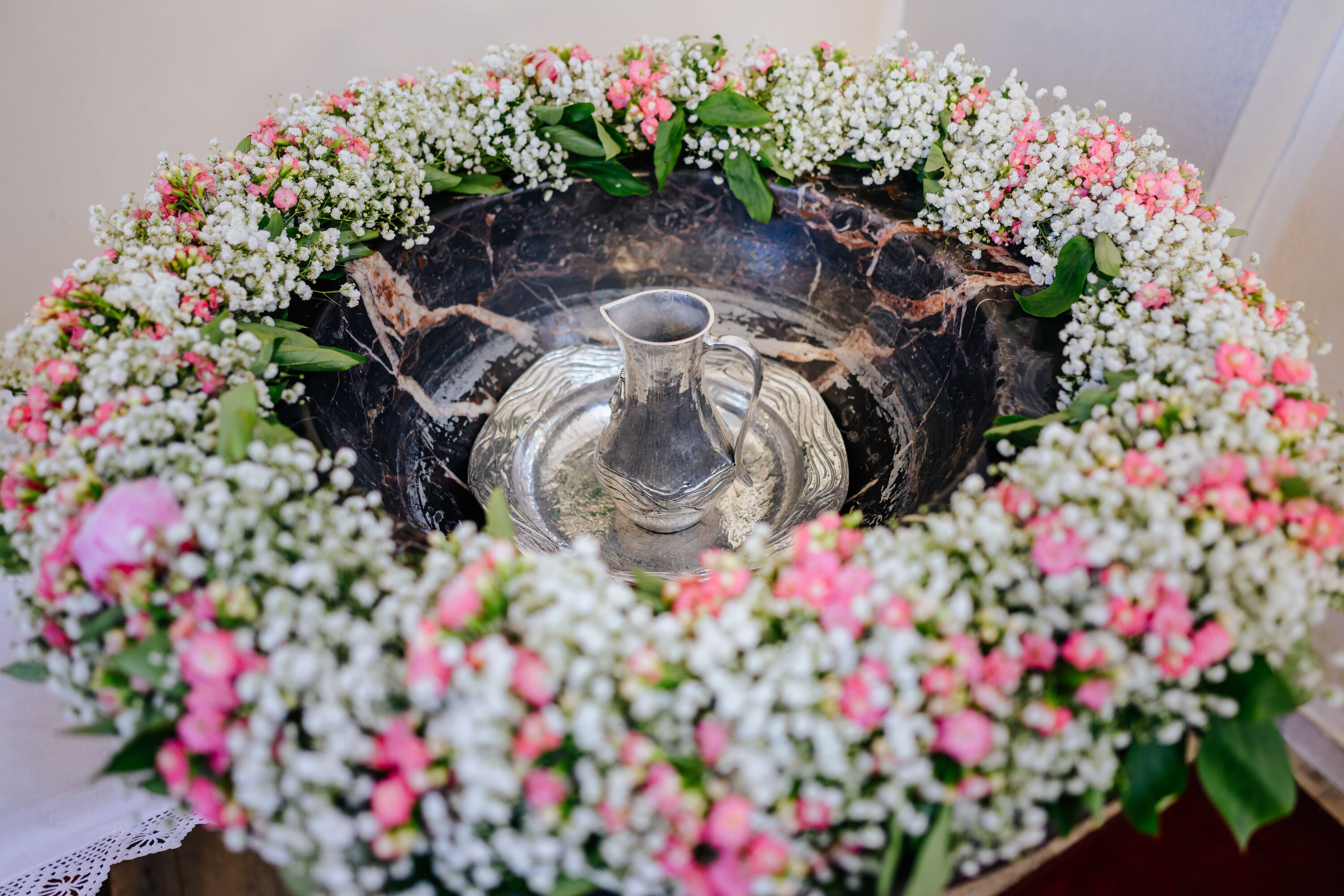 Taufbecken mit Blumenkranz und Kanne.